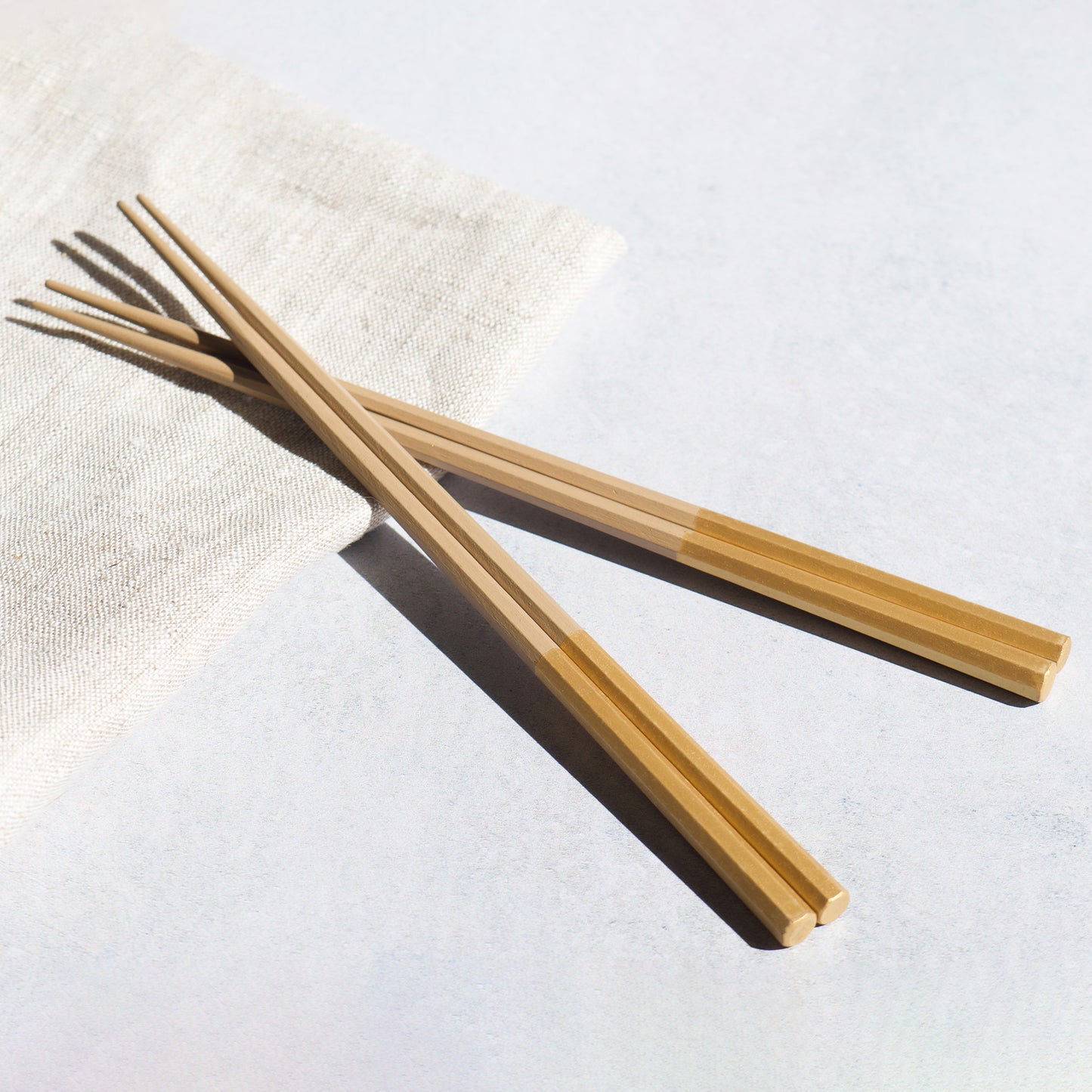 A pair of opulent gold chopsticks, with a lustrous finish, displayed on a linen napkin. Modern Japanese tableware.