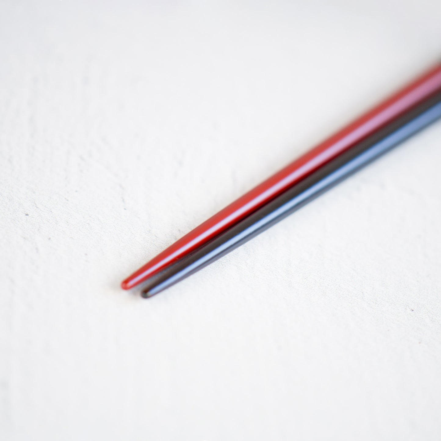 A detailed view of the finely crafted and pointed lacquered heads of the rouge and black chopsticks, designed for effortless and accurate food picking.