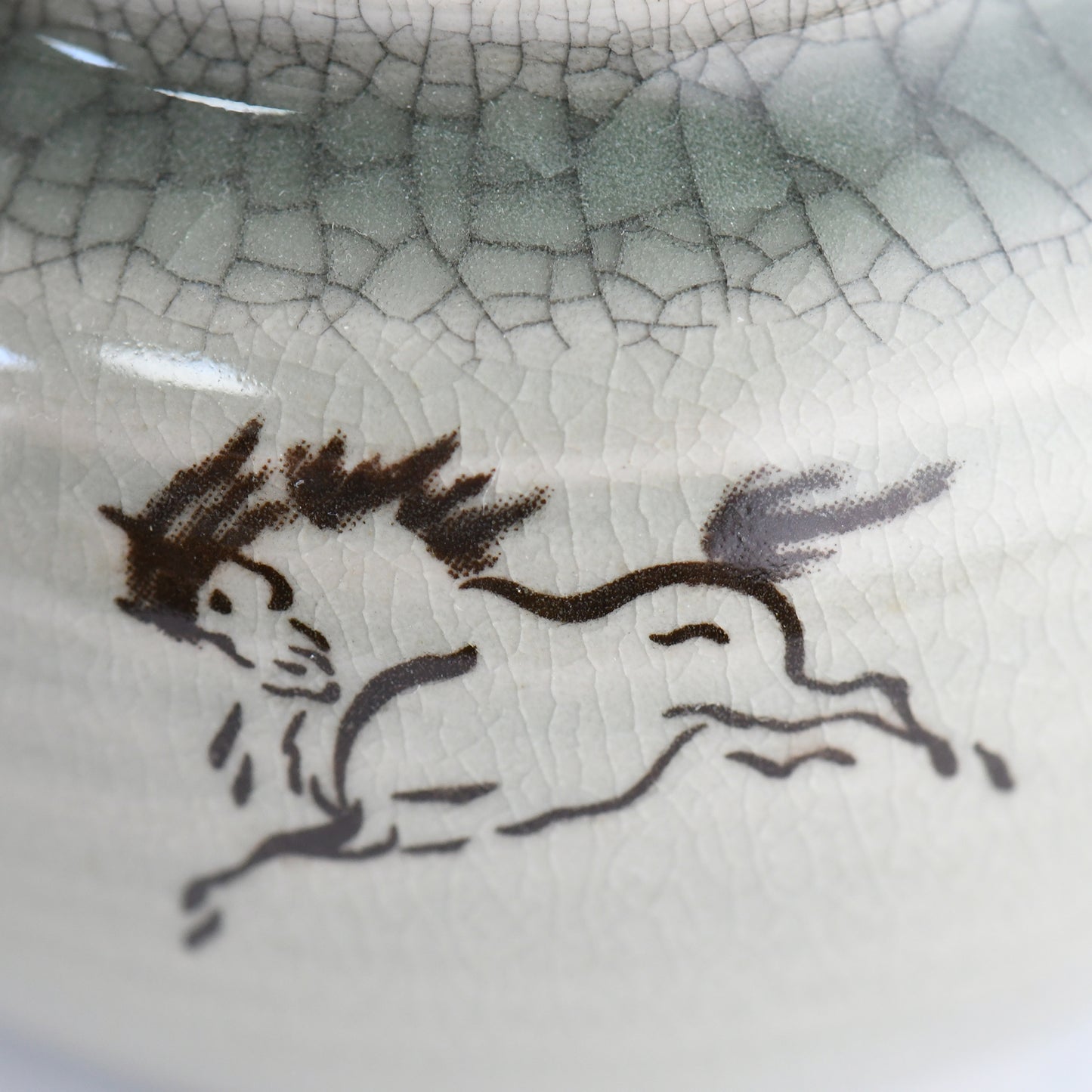 Close-up of hand-painted 左馬 horse design on celadon teapot, symbol of good fortune.