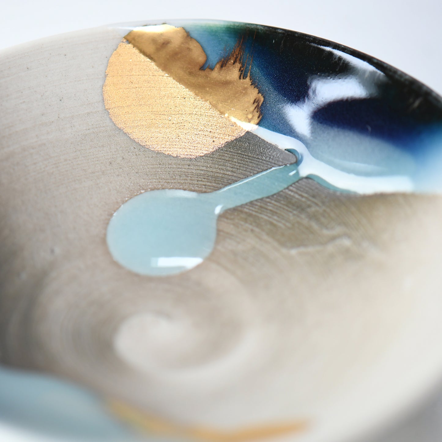Interior view of the sake cup with swirling celadon glaze and radiant gold brushwork.