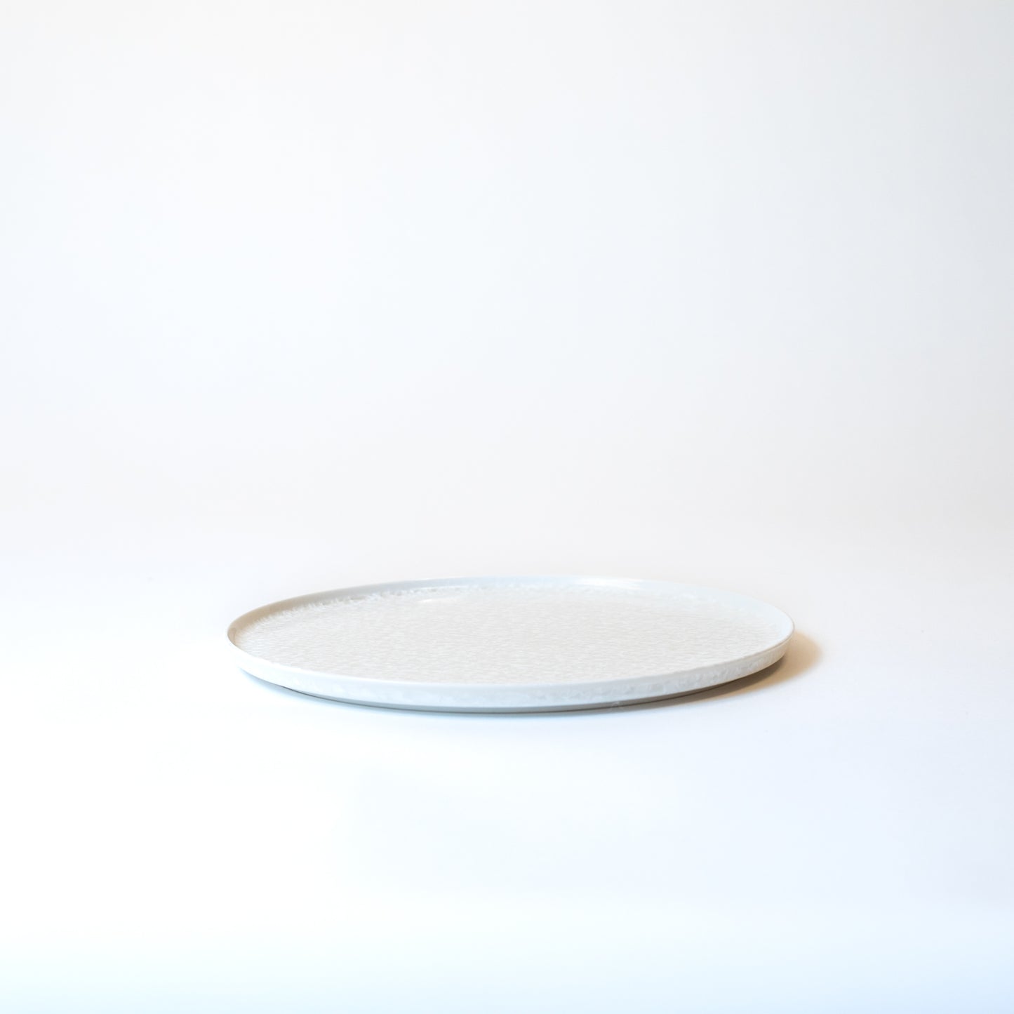 Plate viewed from an angle. About 0.6 inches high. Simple and sleek flat plate.