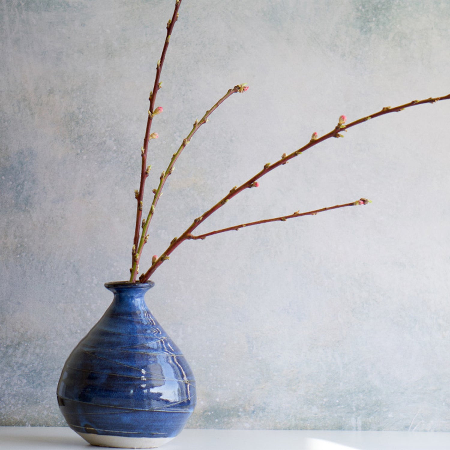 Handmade Japanese vase Miyabi (雅) with deep indigo glaze, displayed with budding branches in a minimalist setting.