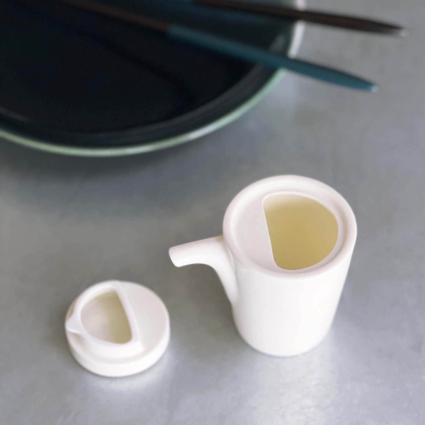 White, cylindrical designed shoyu container designed with a tab securing the cover while pouring