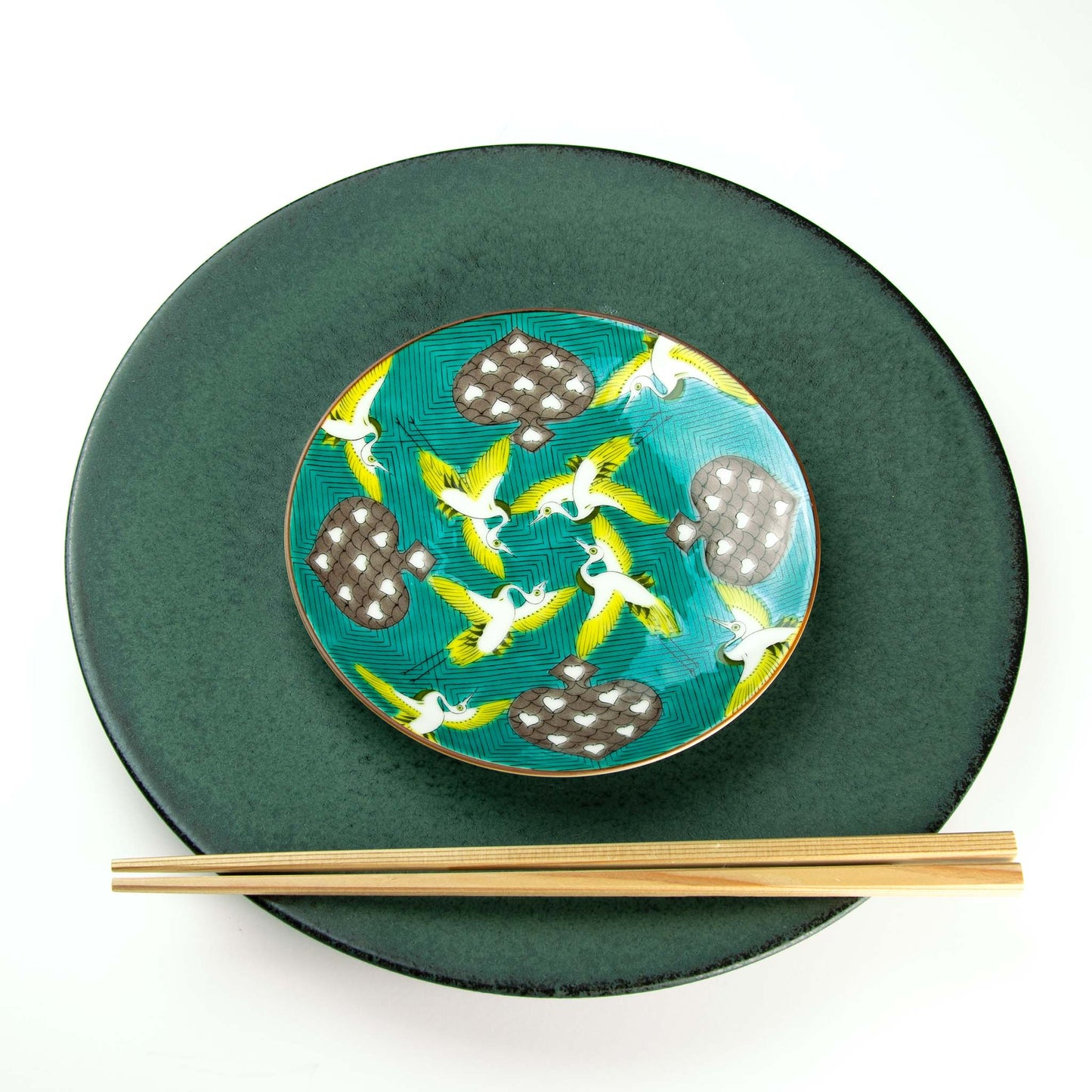 Yellow and white birds flying among spades set on a green background of yellow and blue waves. Paired with Koku dinnerware.