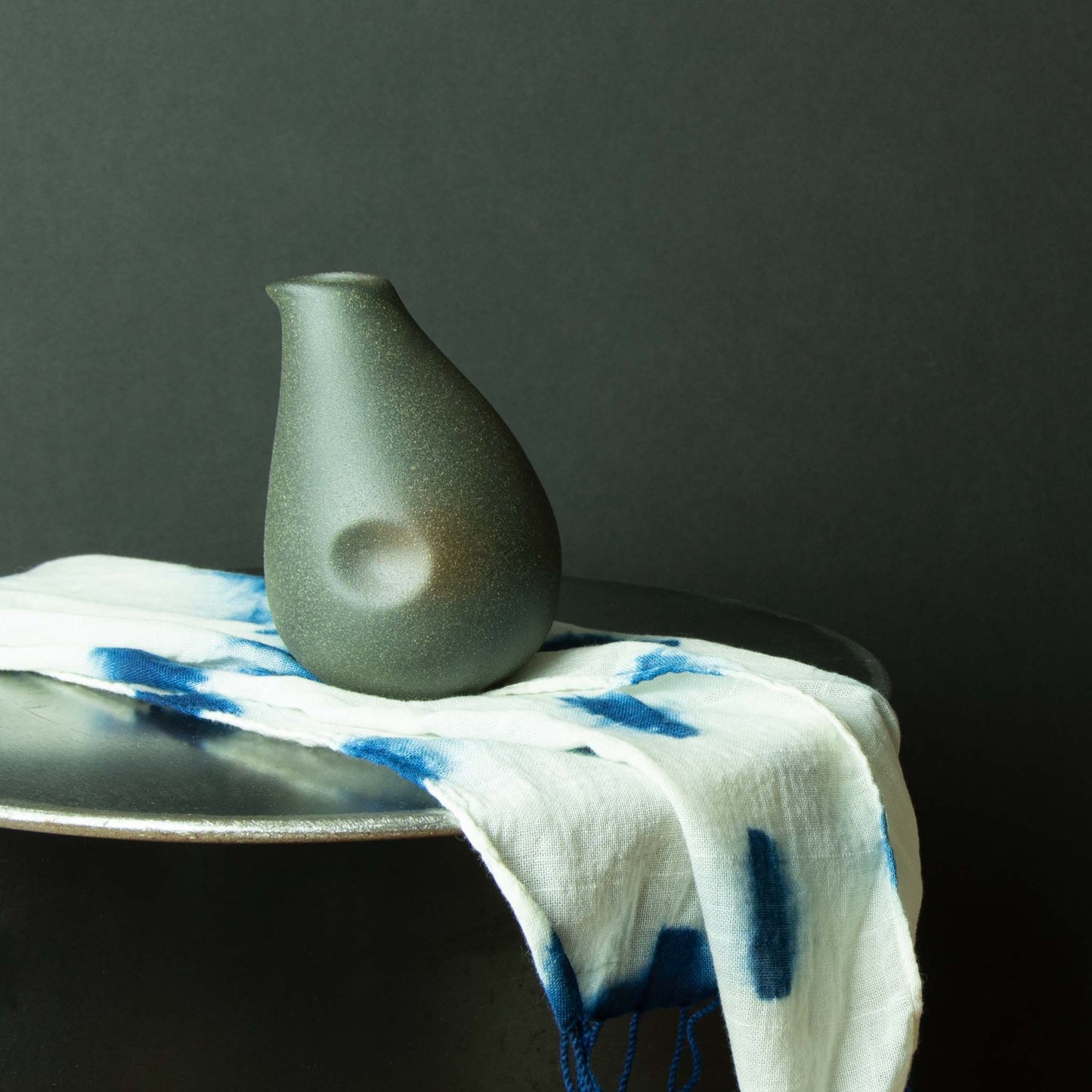 Speckled dark grey sake container with opening to the side with dimple for thumb.