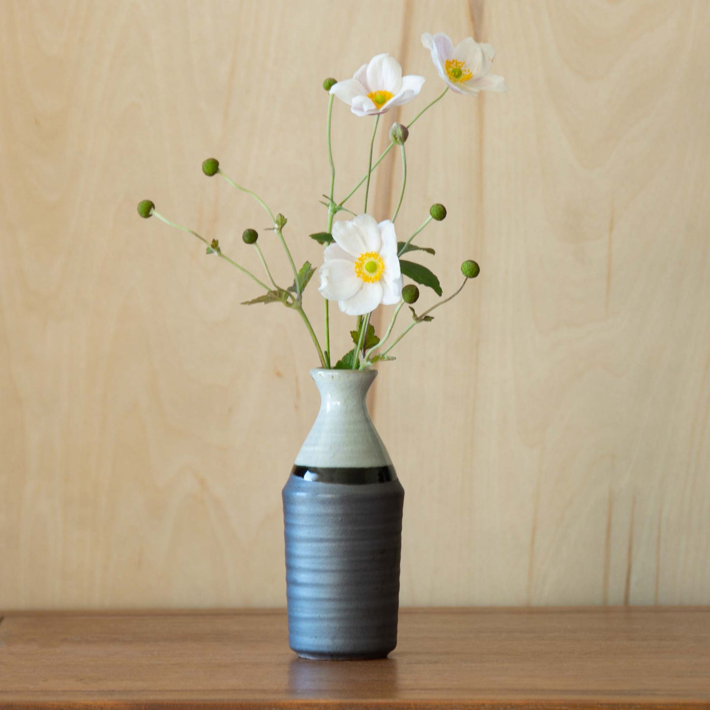 Grey and white sake container vase with green foliage combined with white camelia