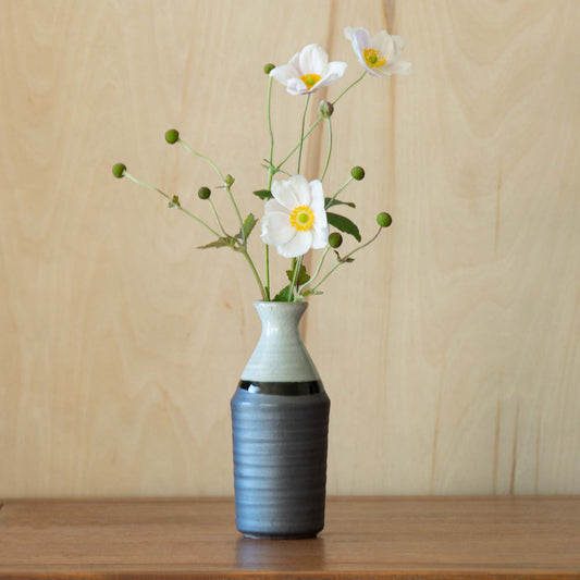 Grey and white sake container vase with green foliage combined with white camelia