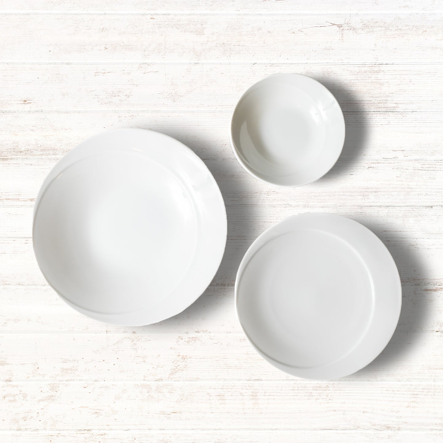 A 3-piece white dinnerware set including a deep plate, a salad plate, and a small bowl, displayed on a wooden surface.