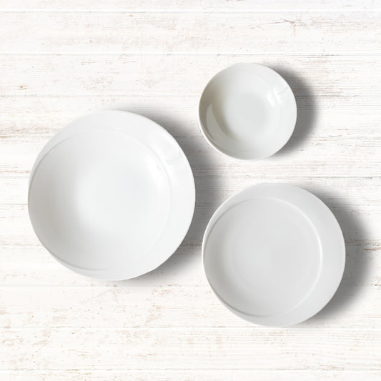 A 3-piece white dinnerware set including a deep plate, a salad plate, and a small bowl, displayed on a wooden surface.