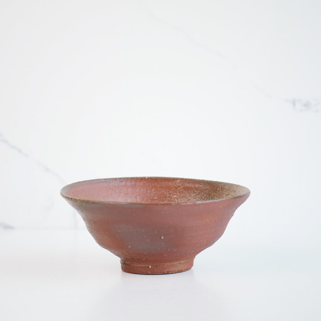 A close-up shot of the elegant rice bowl, showcasing its unique and graceful shape. The color of the bowl is reddish-brown. Premium Japanese pottery.