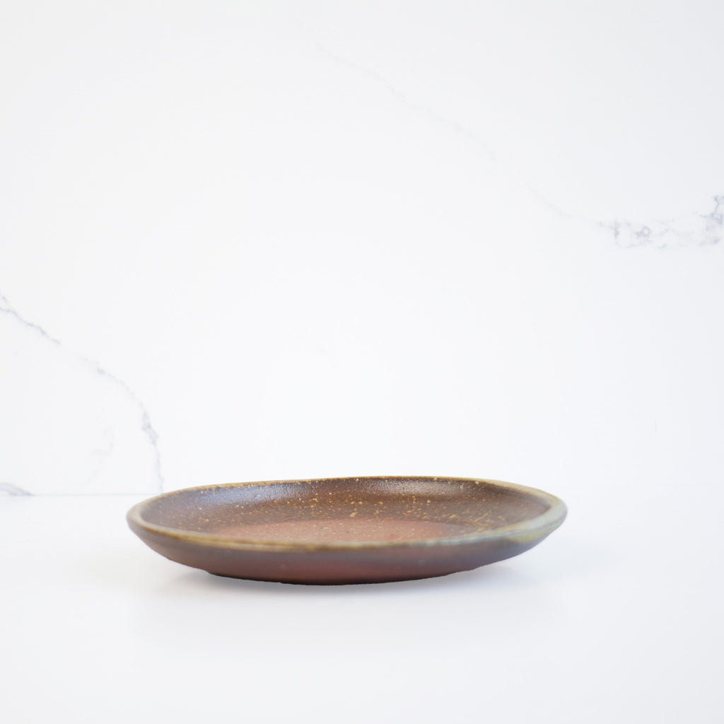 A side view of the plate, emphasizing its naturally curved shape, adding a subtle touch of elegance to the set. Japanese tableware. Wabi-sabi feeling.