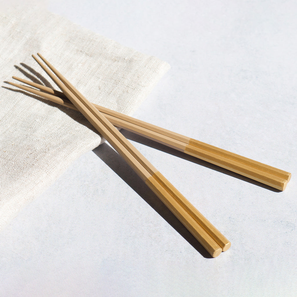 A pair of opulent gold chopsticks, with a lustrous finish, displayed on a linen napkin.  Modern Japanese tableware. 