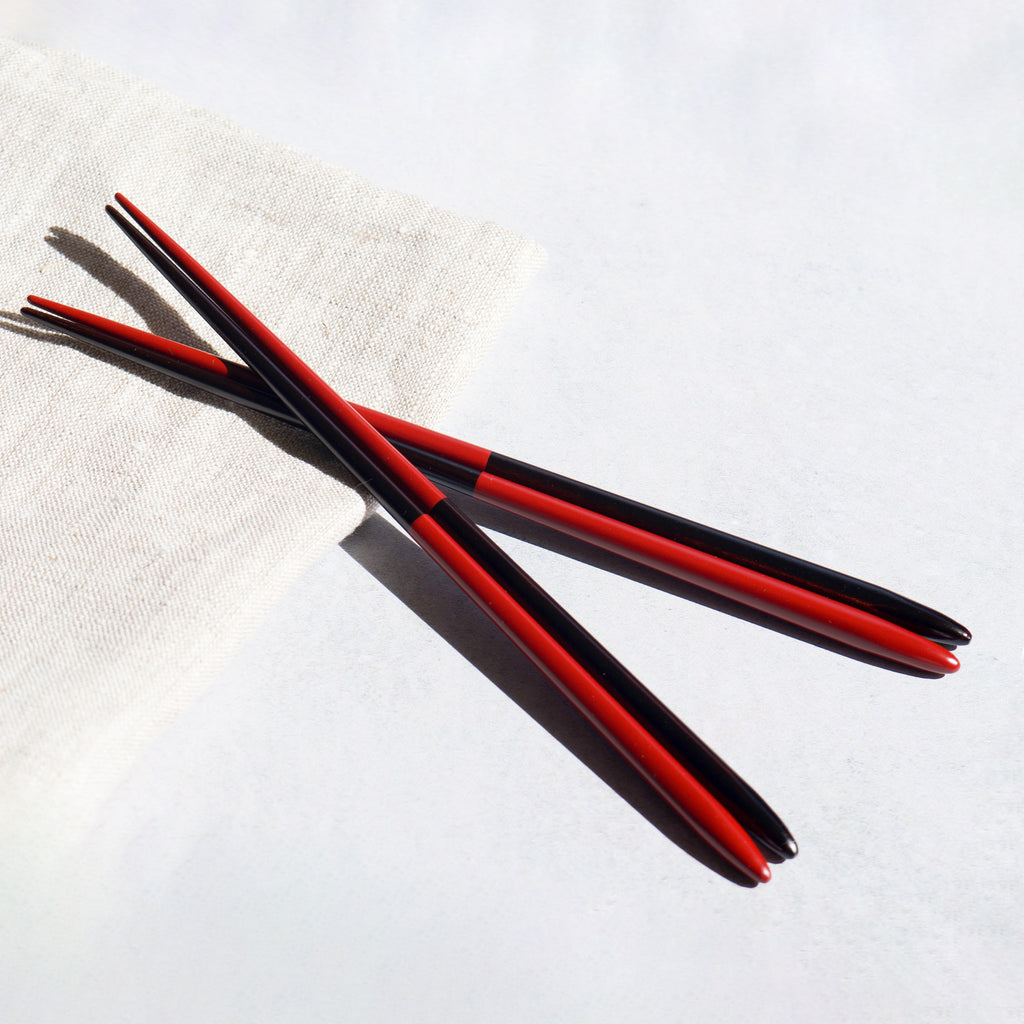 The chic and modern chopsticks with a split half-rouge and half-black lacquered finish, resting on a clean linen napkin. Japan made chopsticks.
