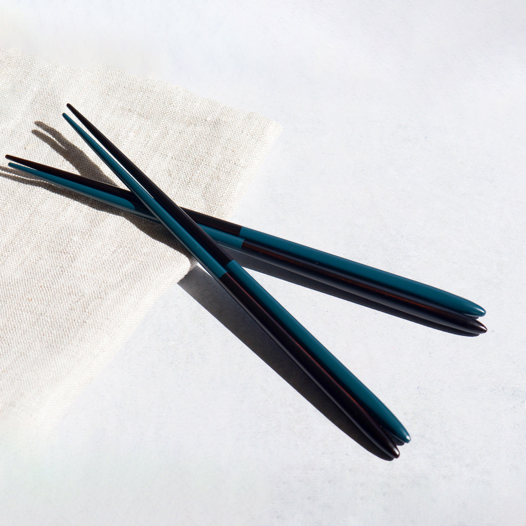 A pair of chopsticks with a striking half-navy and half-black lacquered finish, placed on a crisp white linen napkin. Handmade in Japan. Modern Japanese tableware.