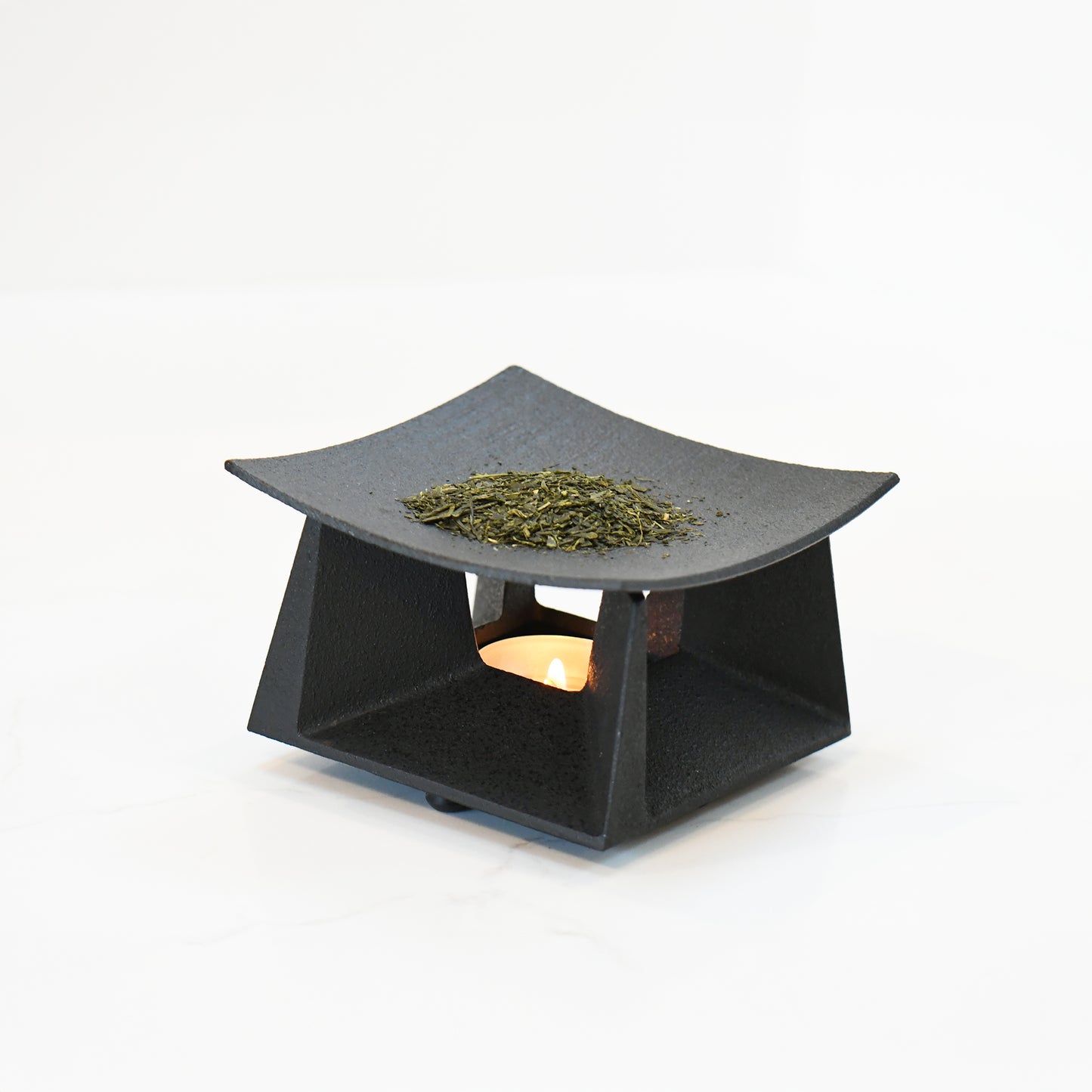 Tea incense burner in use, with loose tea leaves warming above a candle, creating a soft, ambient glow.