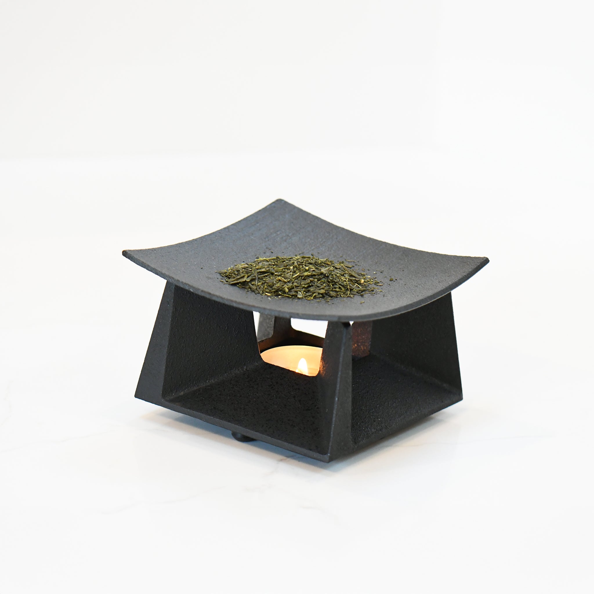 Tea incense burner in use, with loose tea leaves warming above a candle, creating a soft, ambient glow.