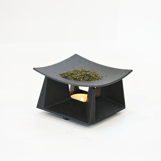 Tea incense burner in use, with loose tea leaves warming above a candle, creating a soft, ambient glow.