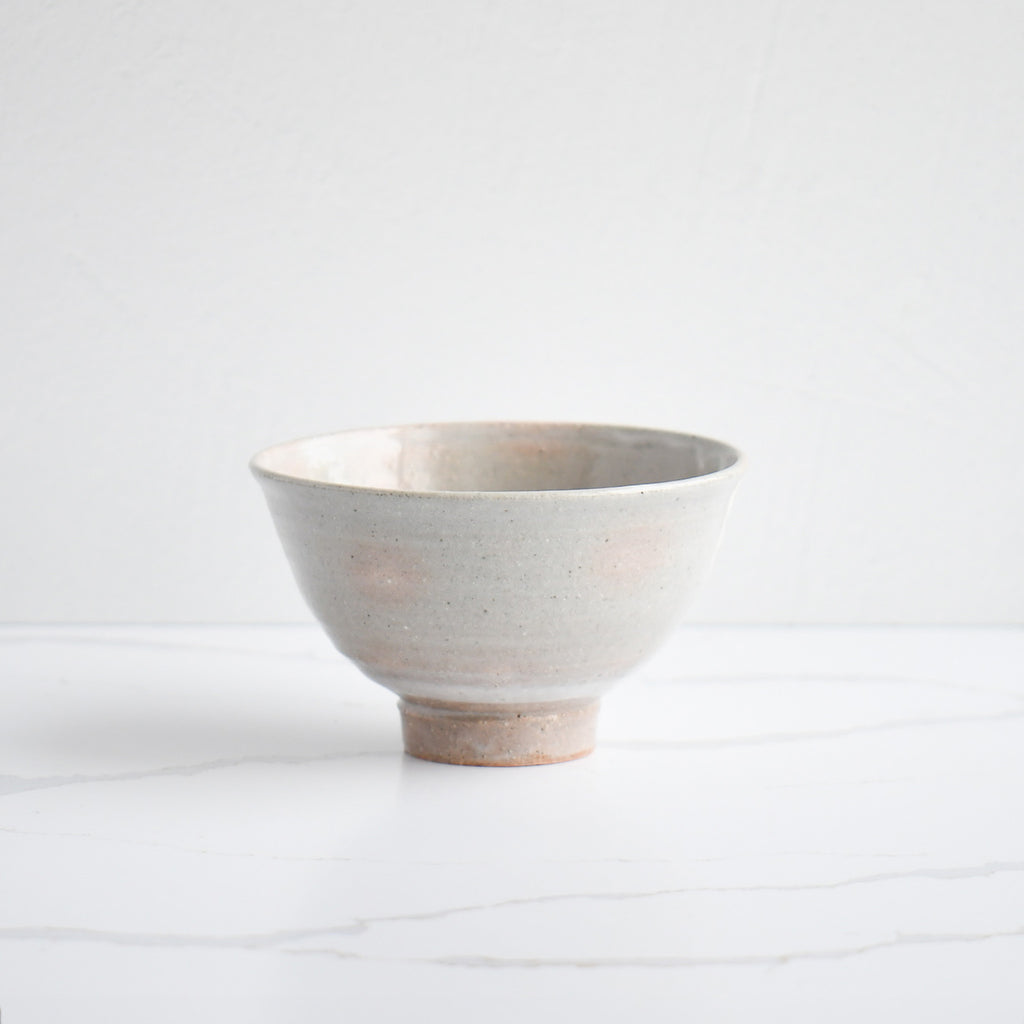 A handmade ceramic bowl with a speckled gray glaze, featuring subtle white drips and a sturdy, unglazed foot.