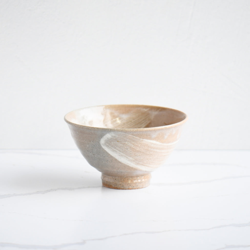 A handcrafted ceramic bowl featuring a swirled pattern in shades of cream and tan with a distinctive brushed texture