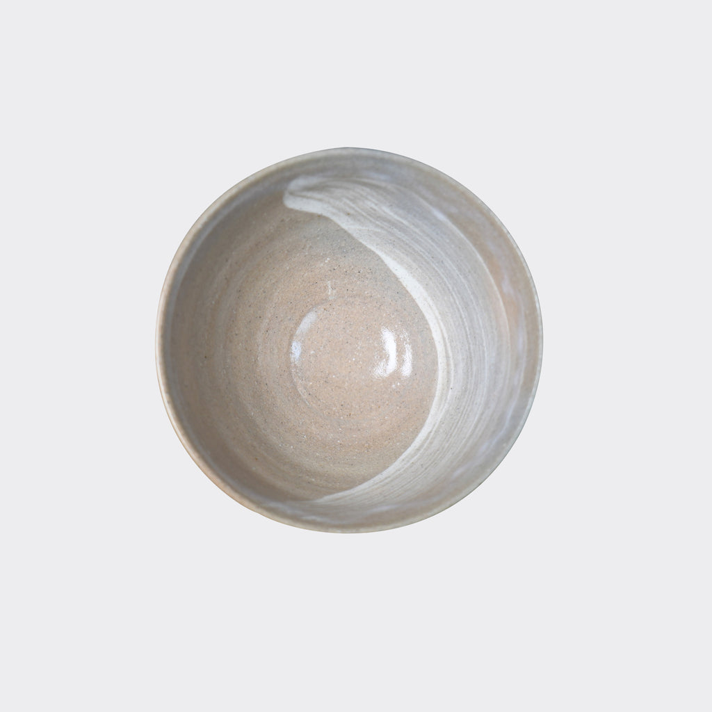 A top-down view of a handcrafted ceramic bowl with a smooth gradient of light gray over a beige base, featuring a swirling white brushed stroke pattern inside.