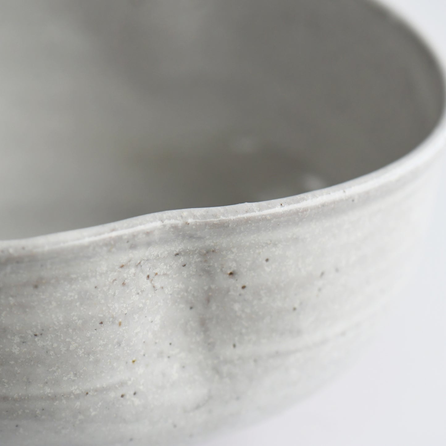 Close-up of softly undulating rim and speckled white glaze surface.