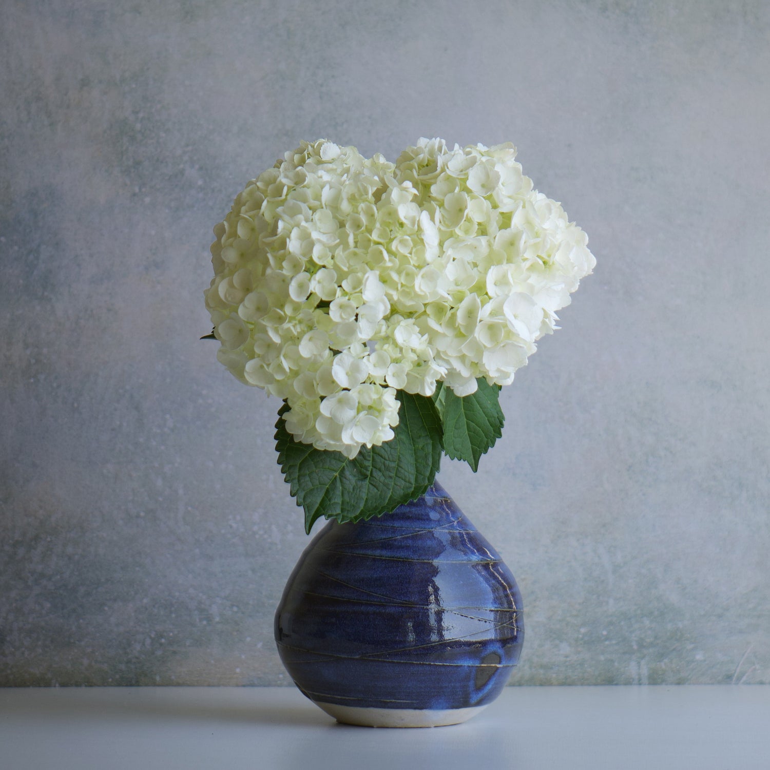 Front view of Miyabi (雅) Japanese vase with white hydrangea, deep indigo glaze, handcrafted from natural soil and glaze.