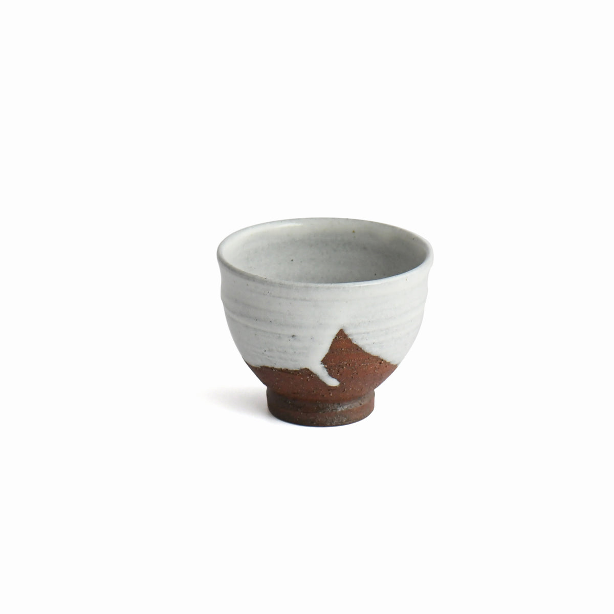 A small handmade ceramic tea cup with a white glazed upper half and a terracotta brown unglazed lower half, shown on a plain white background.