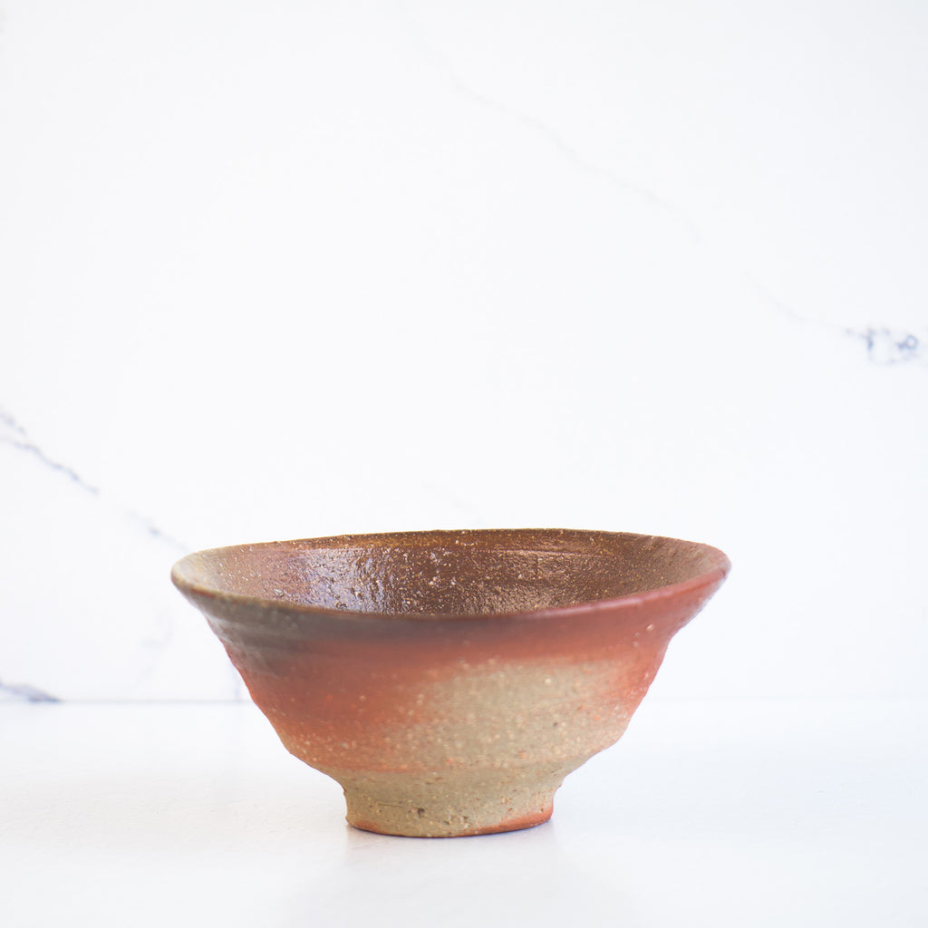 A handmade ceramic rice bowl with a reddish-brown rim and a rustic beige base that adds warmth and texture to any dining experience.