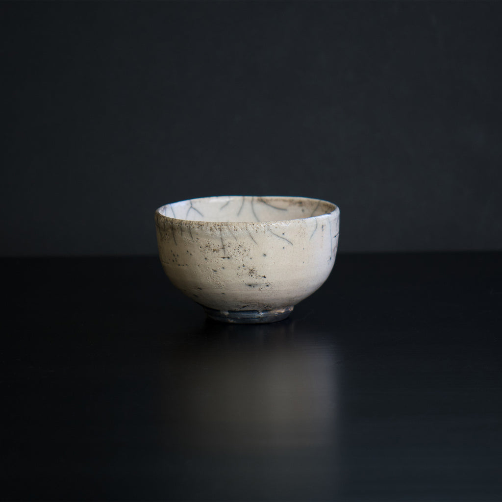 A unique Japanese matcha cup with cream-colored glaze, featuring beautiful gray lines of varying intensity and an original design of black ink-like spots sprinkled throughout.