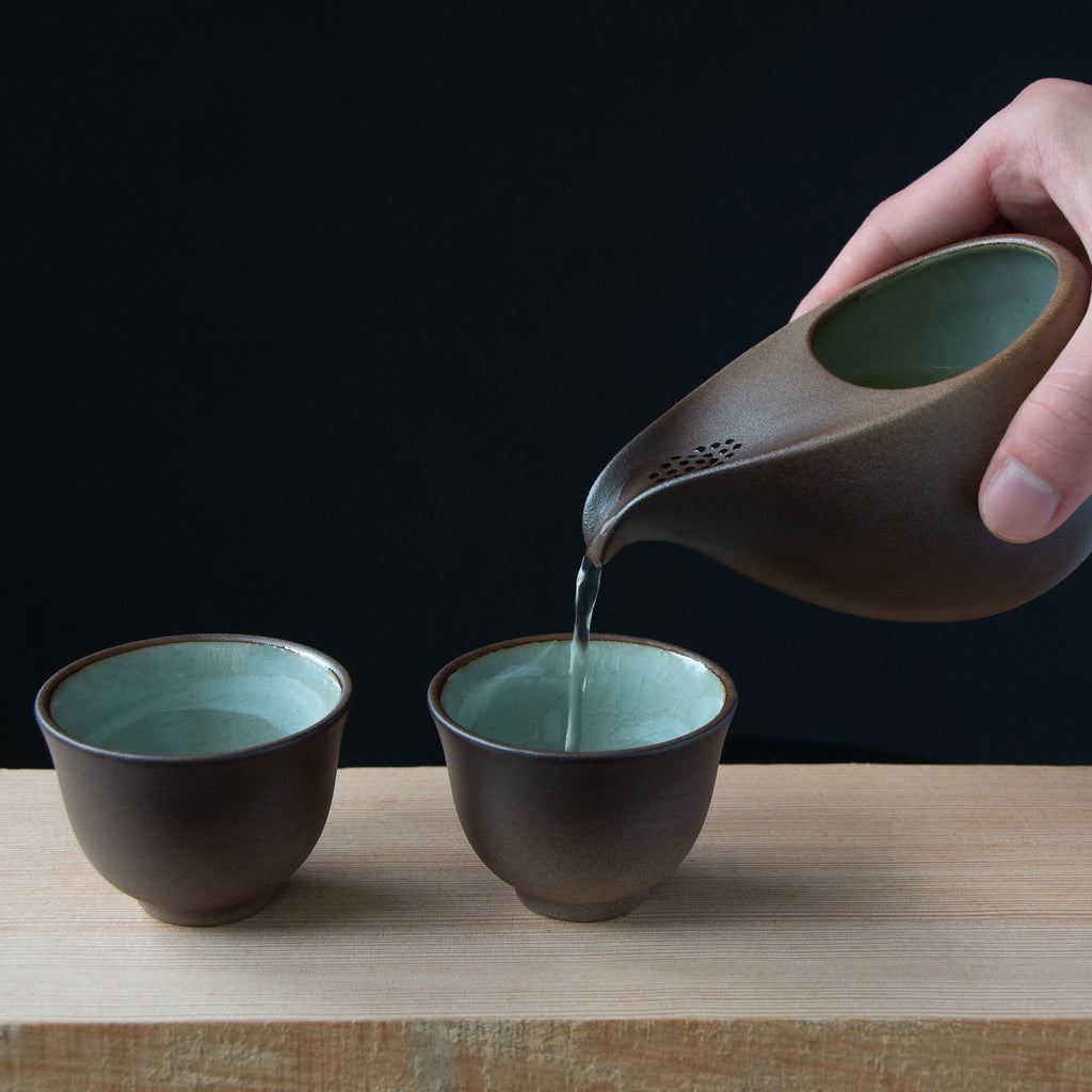 Rich brown gradient surrounds the tea pot and tea cups contrasting with a eucalyptus crackled green glaze