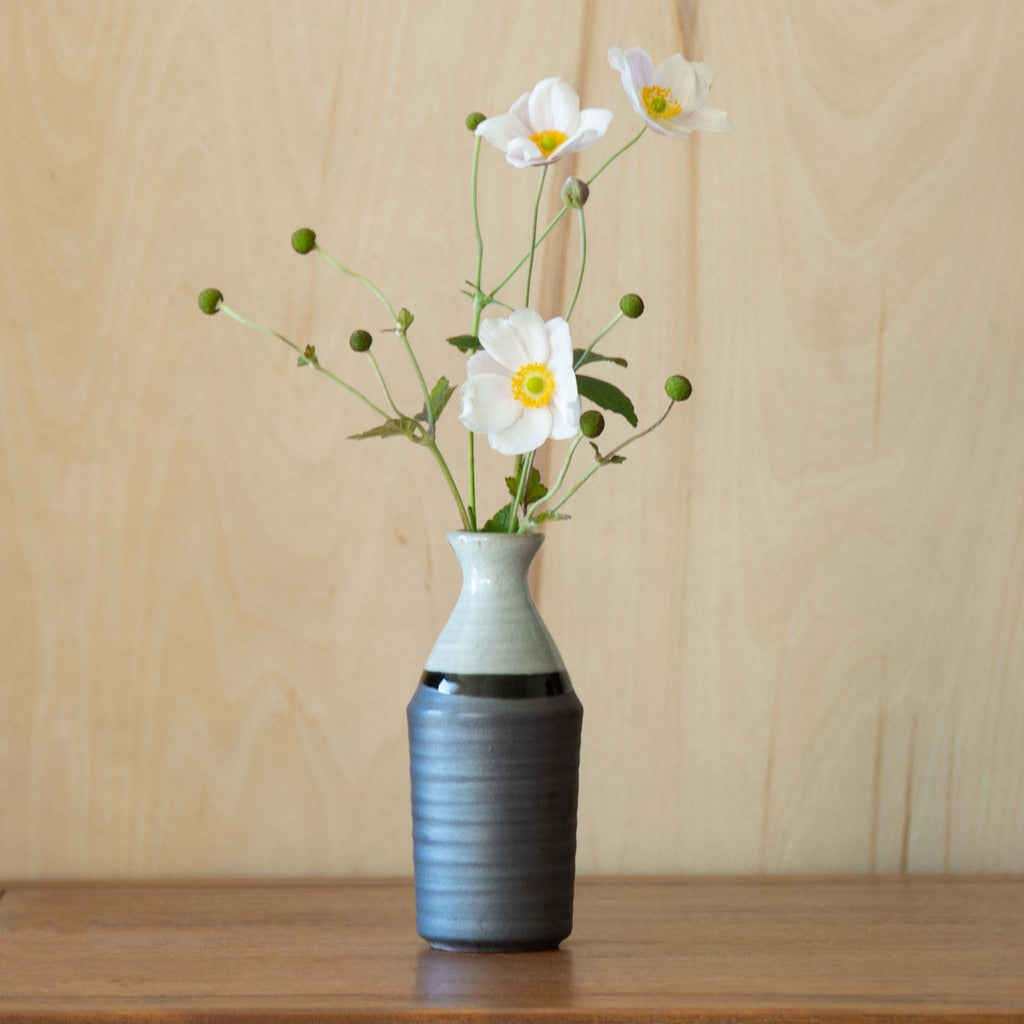 Grey and white sake container vase with green foliage combined with white camelia