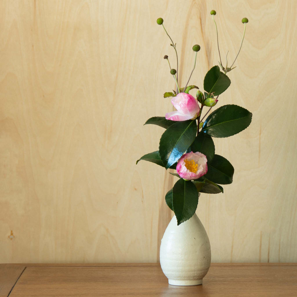 Off-white textured sake container used as vase with green foliage combined with bright pink flowers